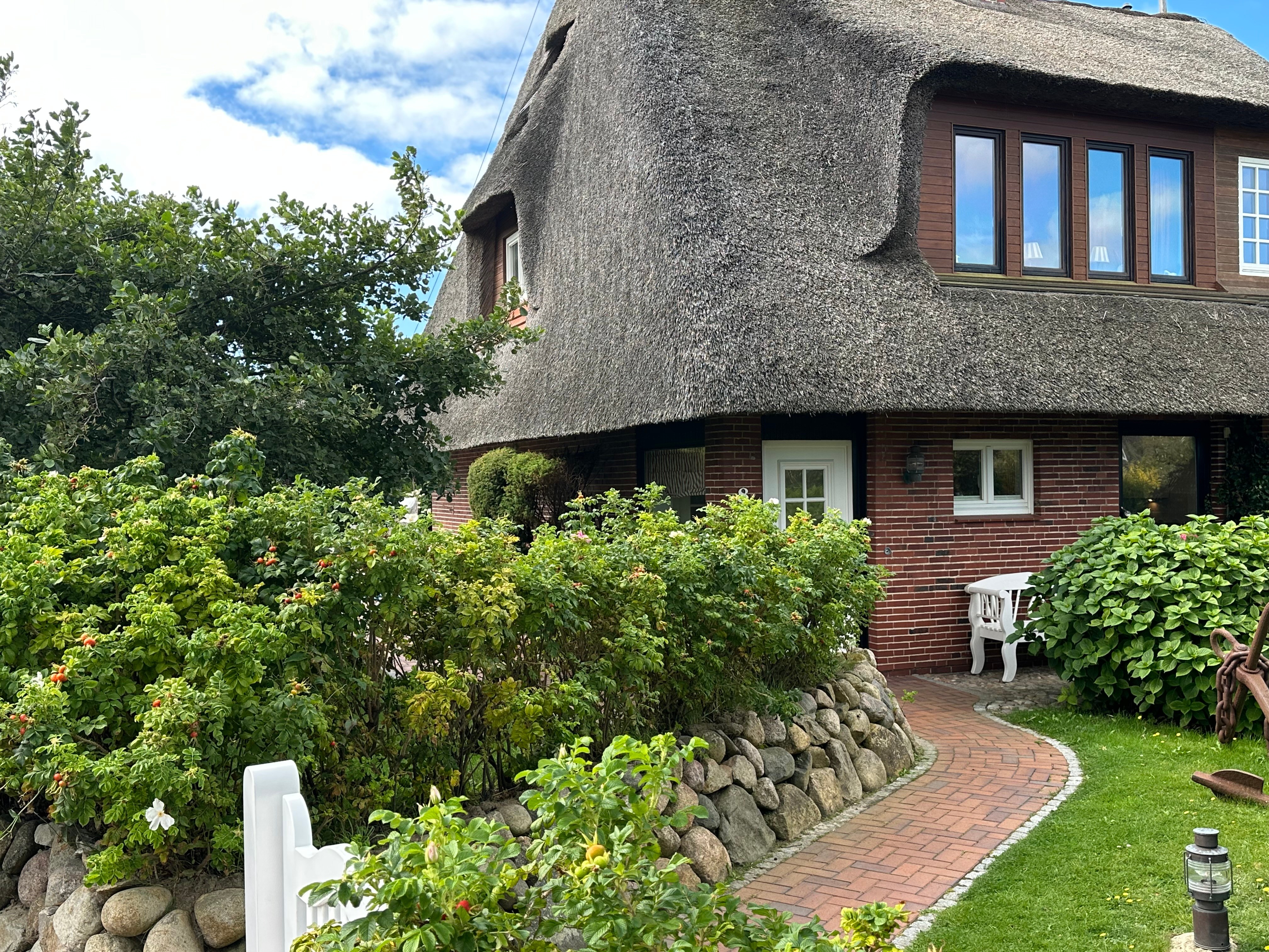 Reetgedecktes Ferienhaus in Wenningstedt auf Sylt mit rotem Klinker, gepflegtem Garten und geschwungenem Klinkerweg.