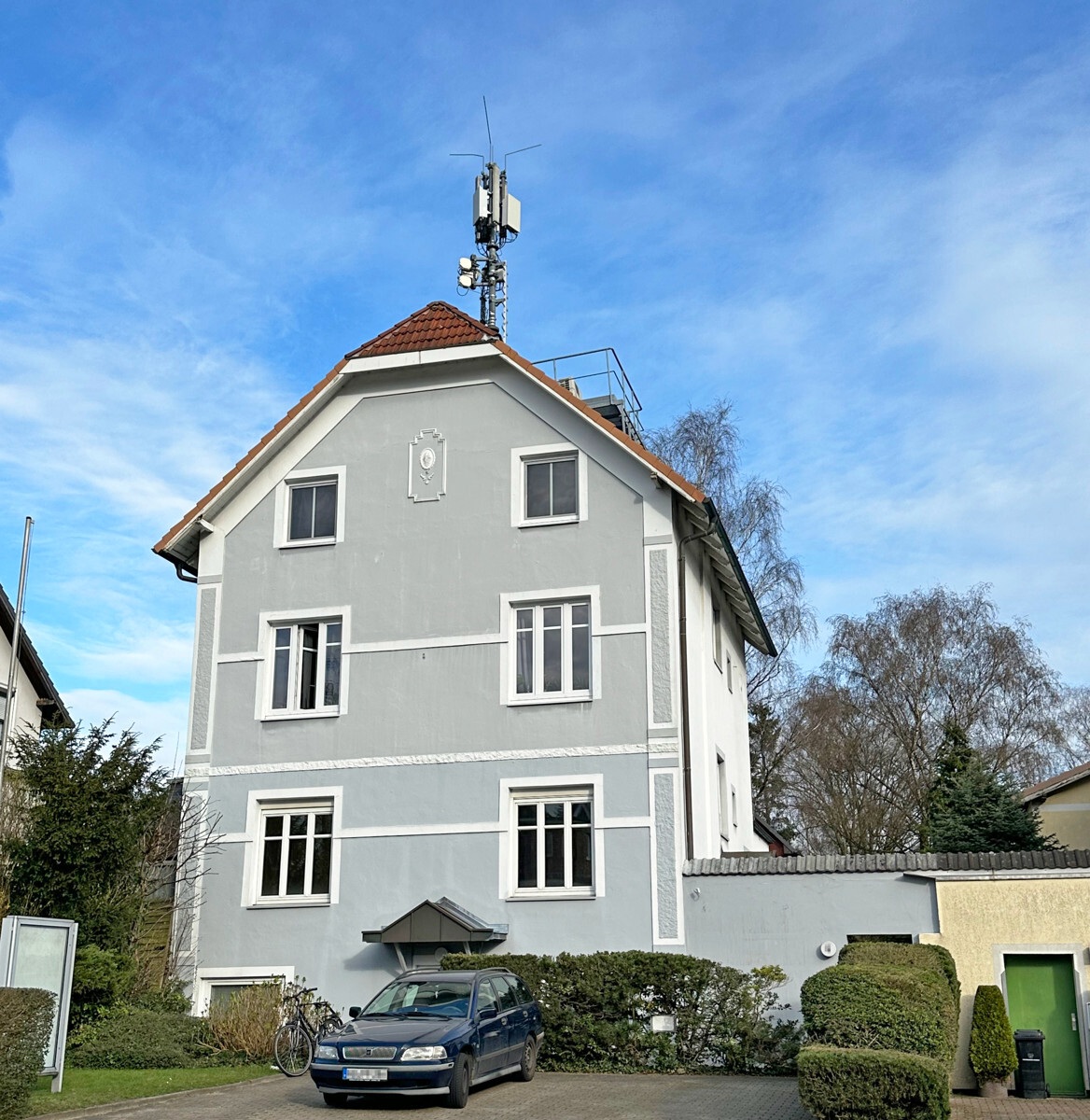 Grau verputztes Mehrfamilienhaus mit weißen Fensterfaschungen und rotem Ziegeldach in Groß Flottbek